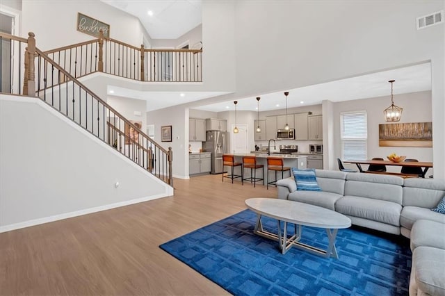 living area with stairway, baseboards, visible vents, light wood-type flooring, and a chandelier