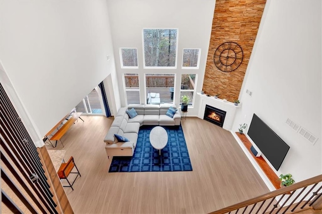 living area featuring visible vents, baseboards, a warm lit fireplace, a high ceiling, and wood finished floors