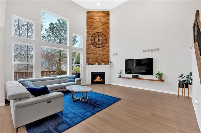 living room featuring wood finished floors, baseboards, visible vents, a high ceiling, and a lit fireplace