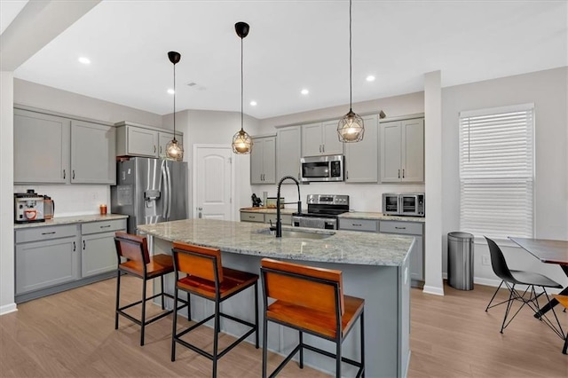 kitchen featuring a sink, a kitchen breakfast bar, appliances with stainless steel finishes, and gray cabinetry