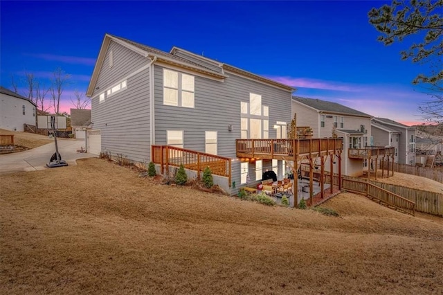 back of house at dusk featuring a wooden deck, a patio, and fence