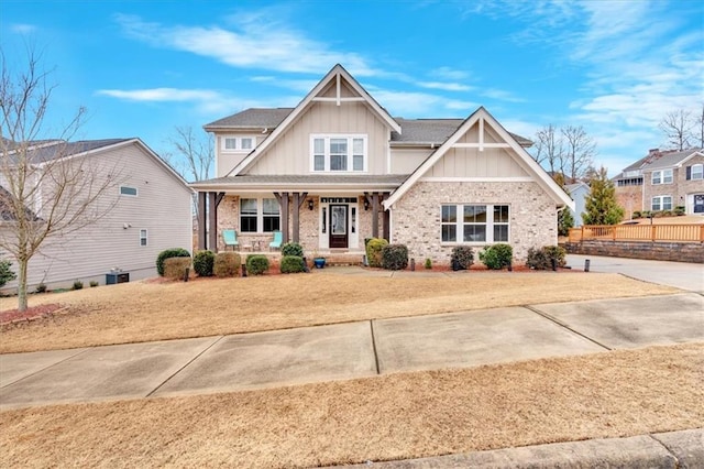 craftsman-style house with brick siding, board and batten siding, a front lawn, a porch, and central AC unit