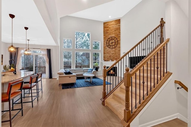 staircase with a large fireplace, baseboards, a high ceiling, and wood finished floors