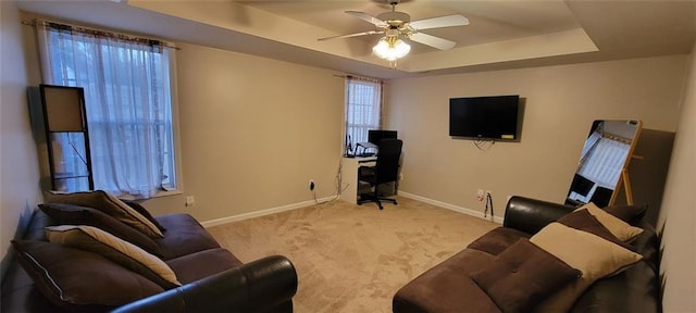 living room featuring a raised ceiling, light colored carpet, and ceiling fan