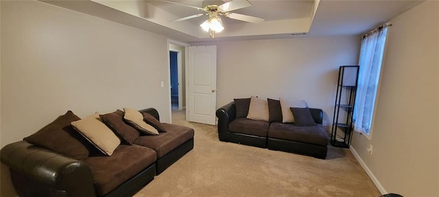 living room with ceiling fan, a raised ceiling, and light carpet