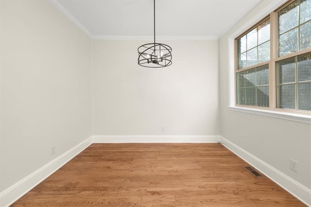 unfurnished dining area featuring hardwood / wood-style floors, crown molding, and a notable chandelier