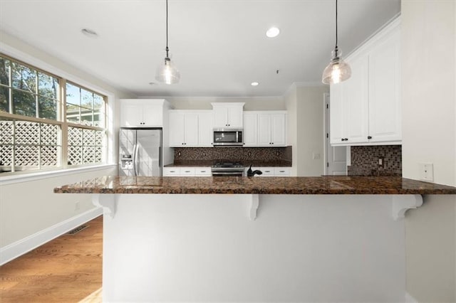 kitchen featuring a breakfast bar area, white cabinetry, hanging light fixtures, and stainless steel appliances