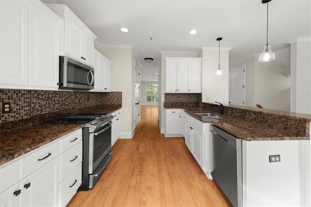 kitchen featuring pendant lighting, white cabinets, crown molding, light wood-type flooring, and stainless steel appliances