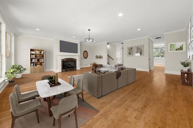 living room with a chandelier, light wood-type flooring, crown molding, and a premium fireplace