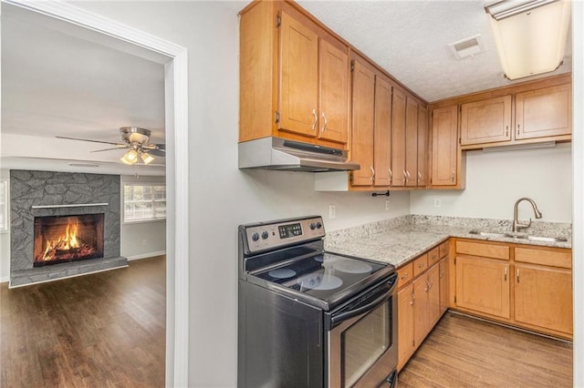 kitchen featuring stainless steel range with electric stovetop, under cabinet range hood, a sink, wood finished floors, and a ceiling fan