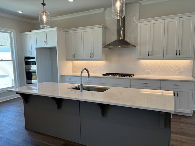 kitchen with pendant lighting, a kitchen island with sink, white cabinets, wall chimney range hood, and sink