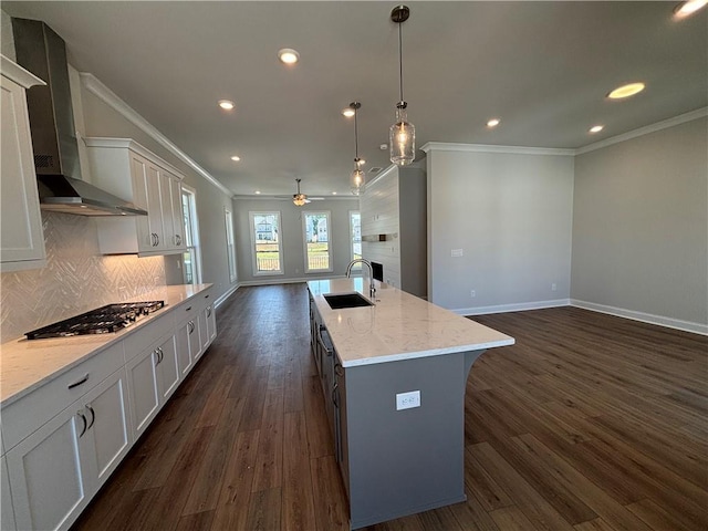 kitchen featuring sink, wall chimney range hood, stainless steel gas cooktop, dark hardwood / wood-style floors, and an island with sink