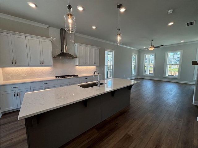 kitchen with pendant lighting, a spacious island, wall chimney range hood, sink, and dark hardwood / wood-style flooring