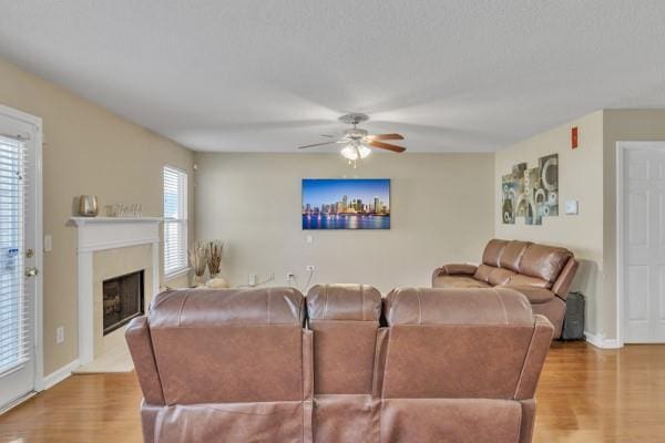 living area with ceiling fan, baseboards, wood finished floors, and a fireplace with raised hearth