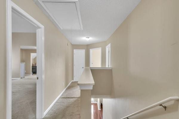 hallway featuring attic access, baseboards, carpet flooring, and an upstairs landing