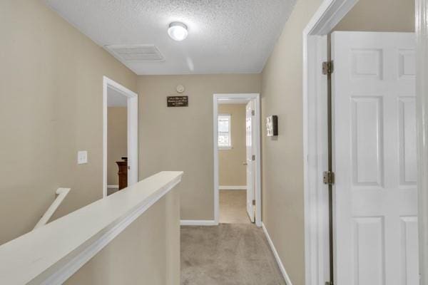 hall with light carpet, baseboards, a textured ceiling, and an upstairs landing