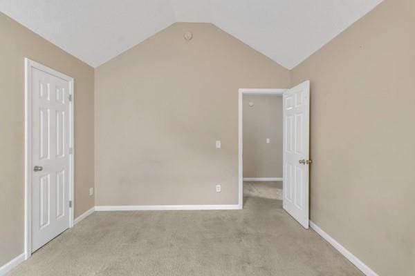 unfurnished bedroom with lofted ceiling, baseboards, and light colored carpet