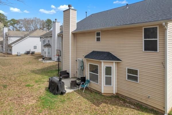 rear view of house with a patio area, a lawn, a chimney, and roof with shingles