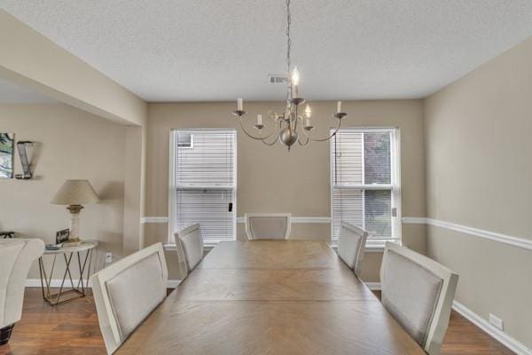 dining area featuring an inviting chandelier, wood finished floors, a textured ceiling, and baseboards