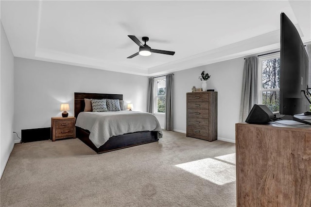 bedroom with a tray ceiling, crown molding, baseboards, light colored carpet, and ceiling fan