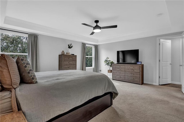 bedroom with a raised ceiling, ornamental molding, baseboards, light colored carpet, and ceiling fan