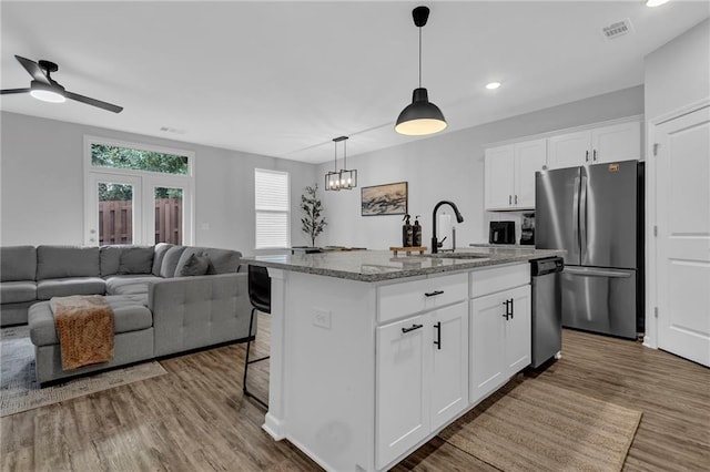 kitchen with wood finished floors, light stone countertops, a sink, hanging light fixtures, and stainless steel appliances