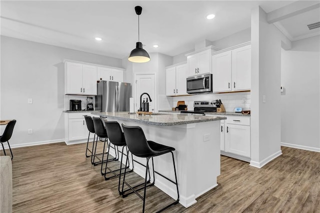 kitchen featuring tasteful backsplash, appliances with stainless steel finishes, a breakfast bar, and wood finished floors