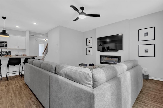 living area featuring a glass covered fireplace, stairway, dark wood-type flooring, and ceiling fan