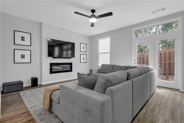 living area with visible vents, baseboards, wood finished floors, a glass covered fireplace, and a ceiling fan