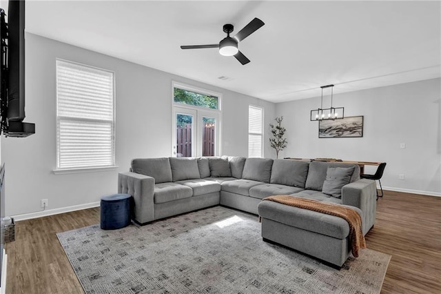 living area with ceiling fan with notable chandelier, baseboards, and wood finished floors