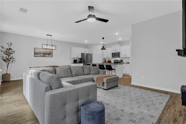 living area featuring visible vents, baseboards, recessed lighting, light wood-style floors, and ceiling fan with notable chandelier