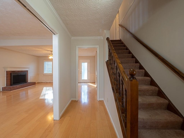 staircase with a textured ceiling, a wainscoted wall, a fireplace, wood finished floors, and ornamental molding