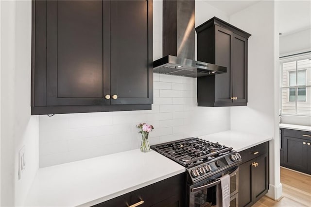 kitchen with wall chimney range hood, gas range, light countertops, and tasteful backsplash