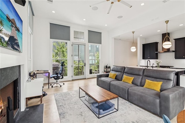 living area featuring a premium fireplace, recessed lighting, light wood-style floors, a ceiling fan, and an office area