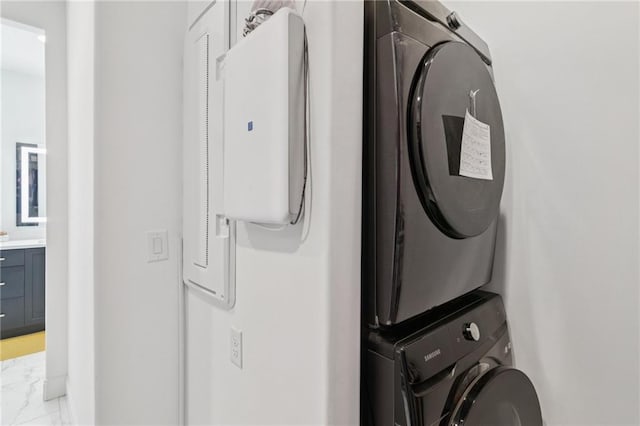 laundry area featuring stacked washer and clothes dryer and light marble finish floors