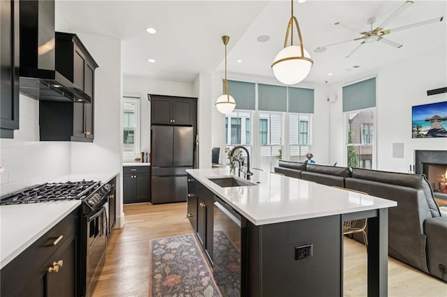 kitchen with appliances with stainless steel finishes, open floor plan, wall chimney range hood, light wood-type flooring, and light countertops