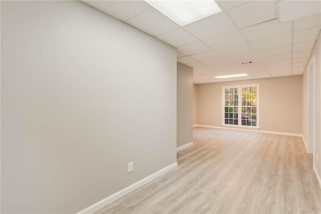 empty room with baseboards, visible vents, a paneled ceiling, and light wood-type flooring