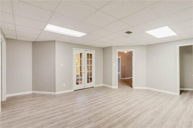 empty room featuring a drop ceiling, visible vents, french doors, light wood-type flooring, and baseboards