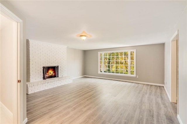 unfurnished living room featuring baseboards, a brick fireplace, and light wood-style flooring
