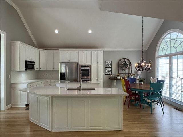 kitchen with lofted ceiling, a center island with sink, stainless steel appliances, and a sink