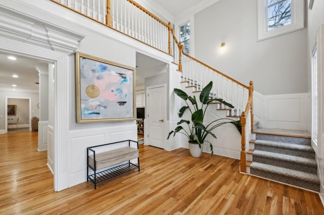 stairway with wood-type flooring, plenty of natural light, a towering ceiling, and ornamental molding