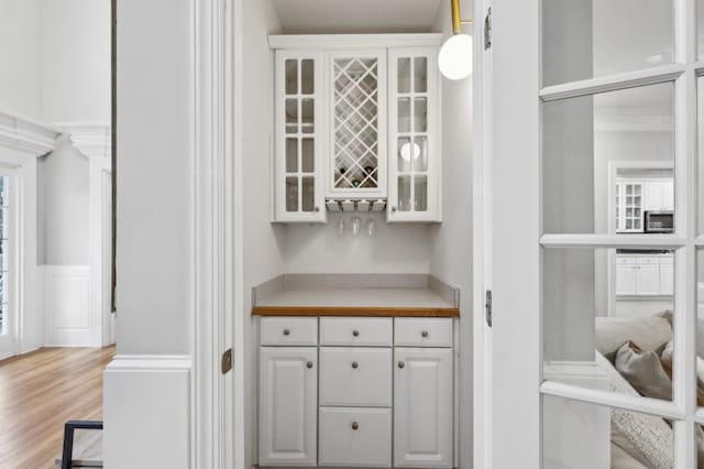 bar featuring hanging light fixtures, white cabinets, and light hardwood / wood-style flooring