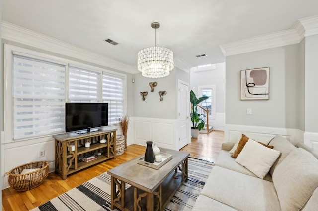 living room with crown molding, an inviting chandelier, and light hardwood / wood-style floors