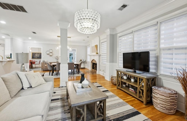 living room featuring an inviting chandelier, ornamental molding, light wood-type flooring, and a wealth of natural light