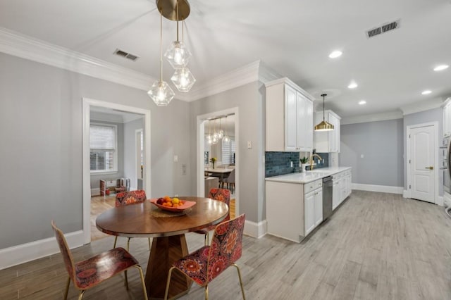 kitchen with white cabinetry, stainless steel dishwasher, ornamental molding, pendant lighting, and light hardwood / wood-style floors