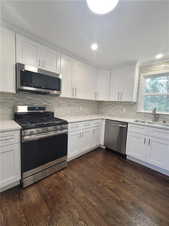 kitchen featuring dark wood-type flooring, stainless steel appliances, tasteful backsplash, white cabinets, and sink