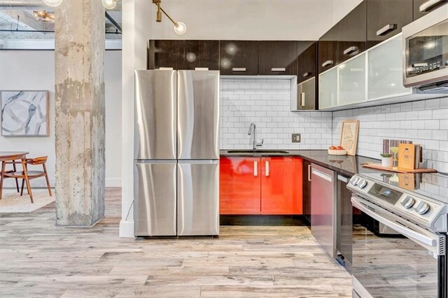 kitchen featuring appliances with stainless steel finishes, dark countertops, a sink, and light wood finished floors