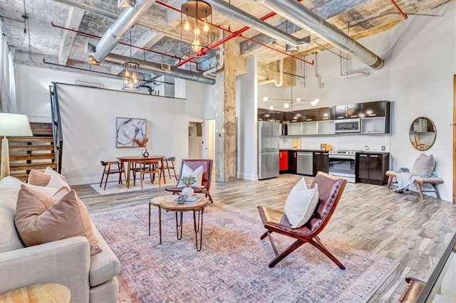 living area with a towering ceiling, light wood-style floors, stairs, and baseboards