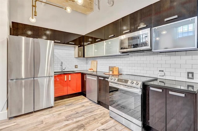 kitchen with a sink, appliances with stainless steel finishes, decorative backsplash, light wood finished floors, and dark countertops