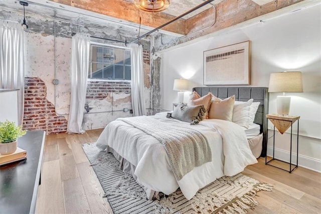 bedroom with brick wall, hardwood / wood-style flooring, and baseboards